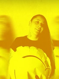 a woman holding a yellow smiley face in front of a yellow background